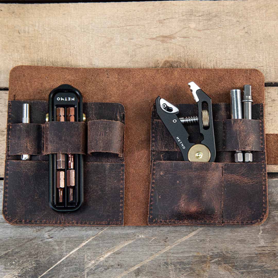 Brown leather multi-tool pouch with various tools on a wooden surface