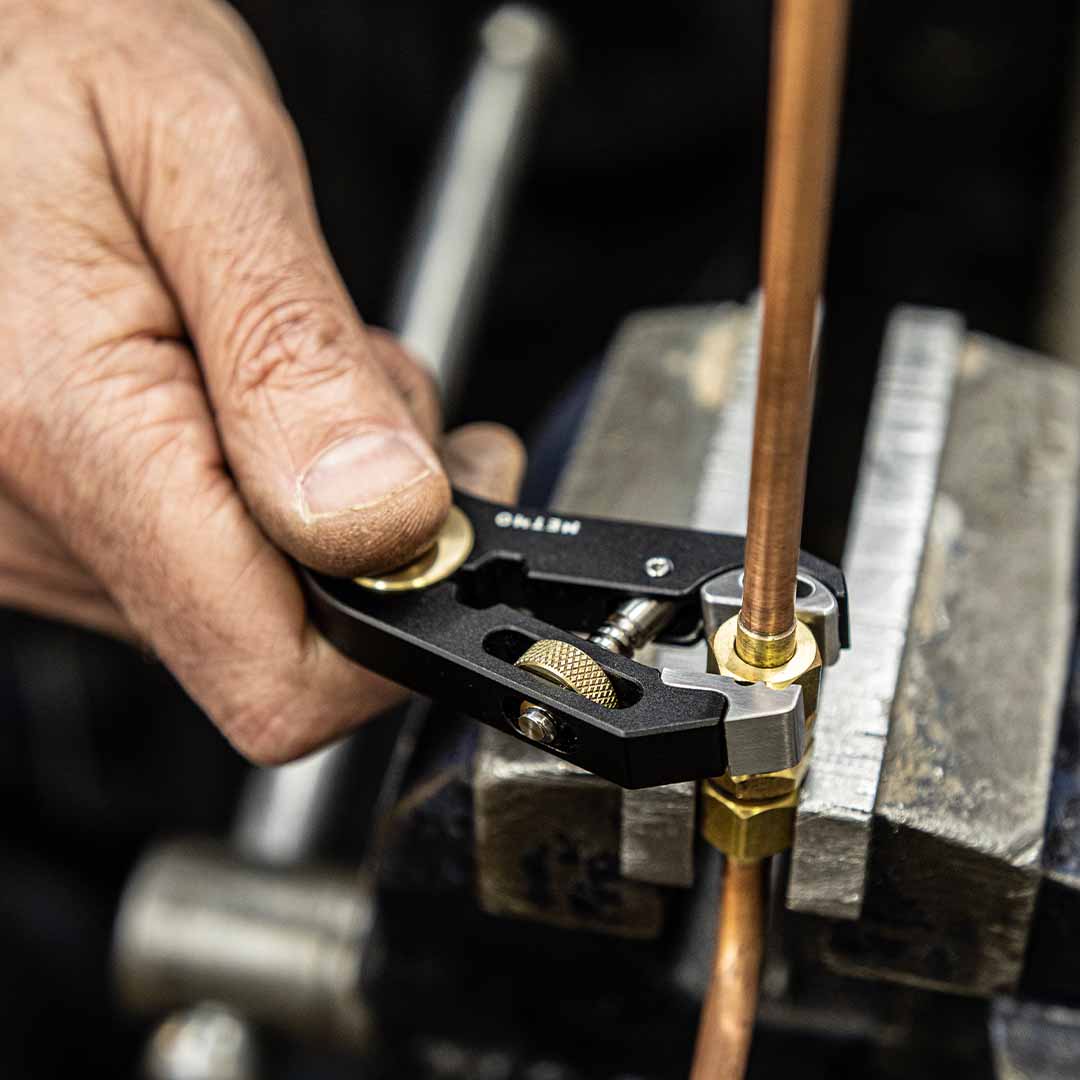 Hand holding a multi tool being used as a wrench for a nut on a copper tube, likely used for precision work.