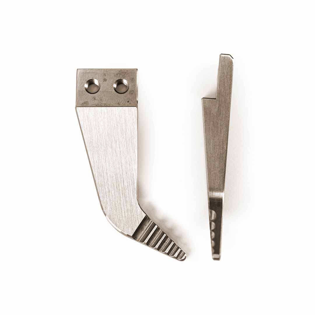 Two silver metal wedge-shaped tool tips with different edge grooves and attachment holes, displayed side-by-side on a plain white background.