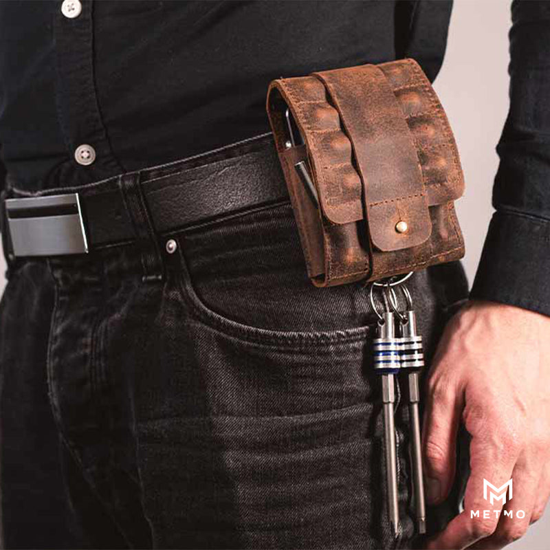 Brown leather pouch on a person's waist with quick release bits attached, wearing black jeans and a dark shirt.