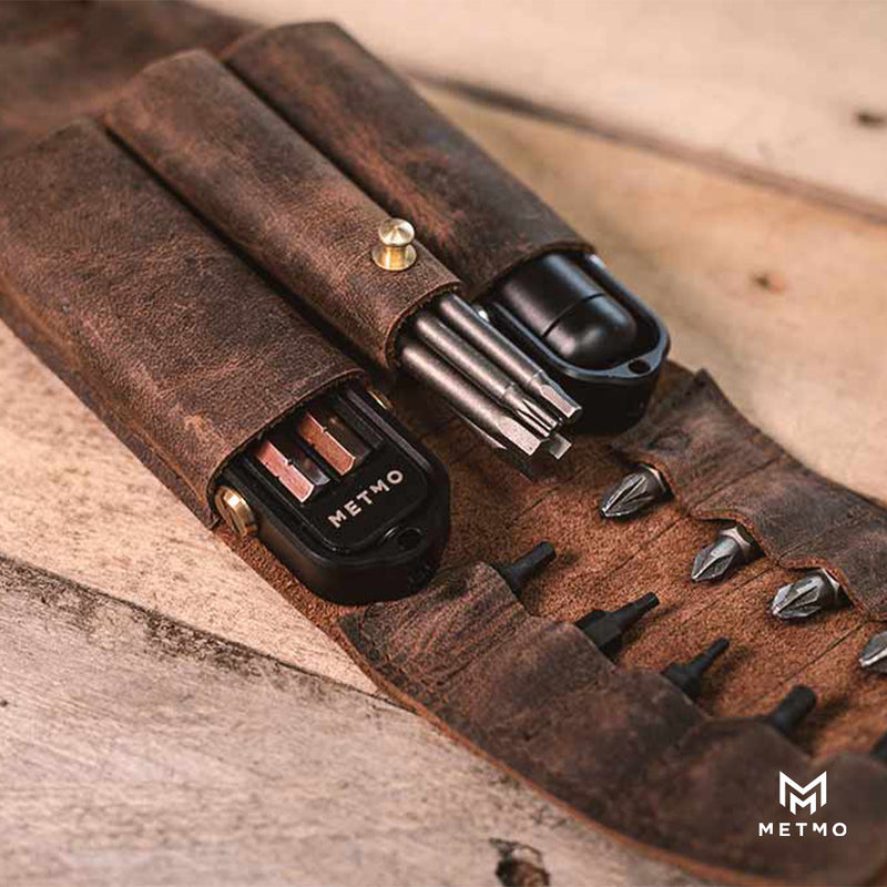 Brown leather tool pouch with black and silver tools and bits on a wooden surface