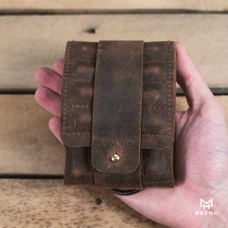 Hand holding a brown leather tool pouch against a wooden background