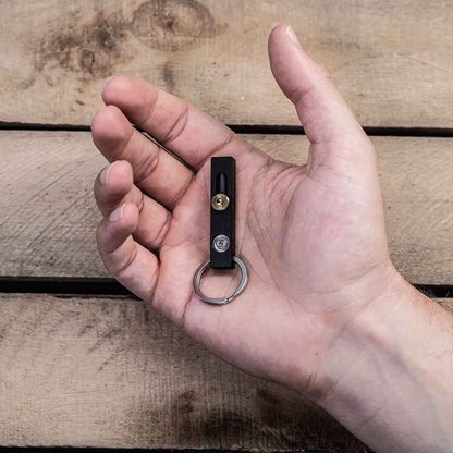 Hand holding a black MetMo Edge with a metal ring on a wooden surface