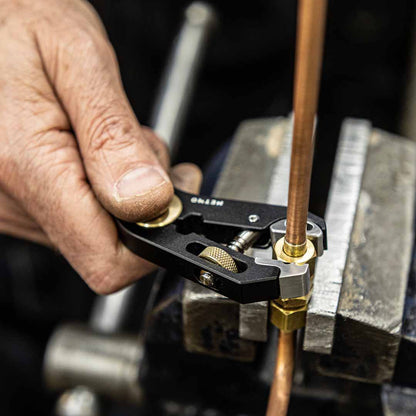 Hand holding a multi tool being used as a wrench for a nut on a copper tube, likely used for precision work.