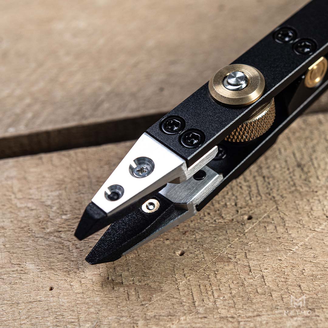 Close-up of a black and silver metal tool with brass-colored screws and a textured gold knob, resting on a rustic wooden surface.