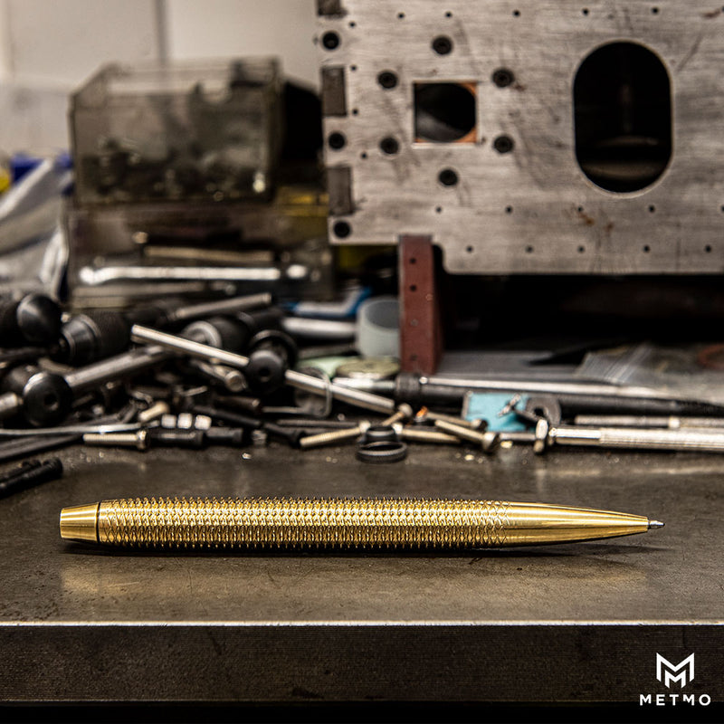 MetMo Brass dual threaded pen on a workbench