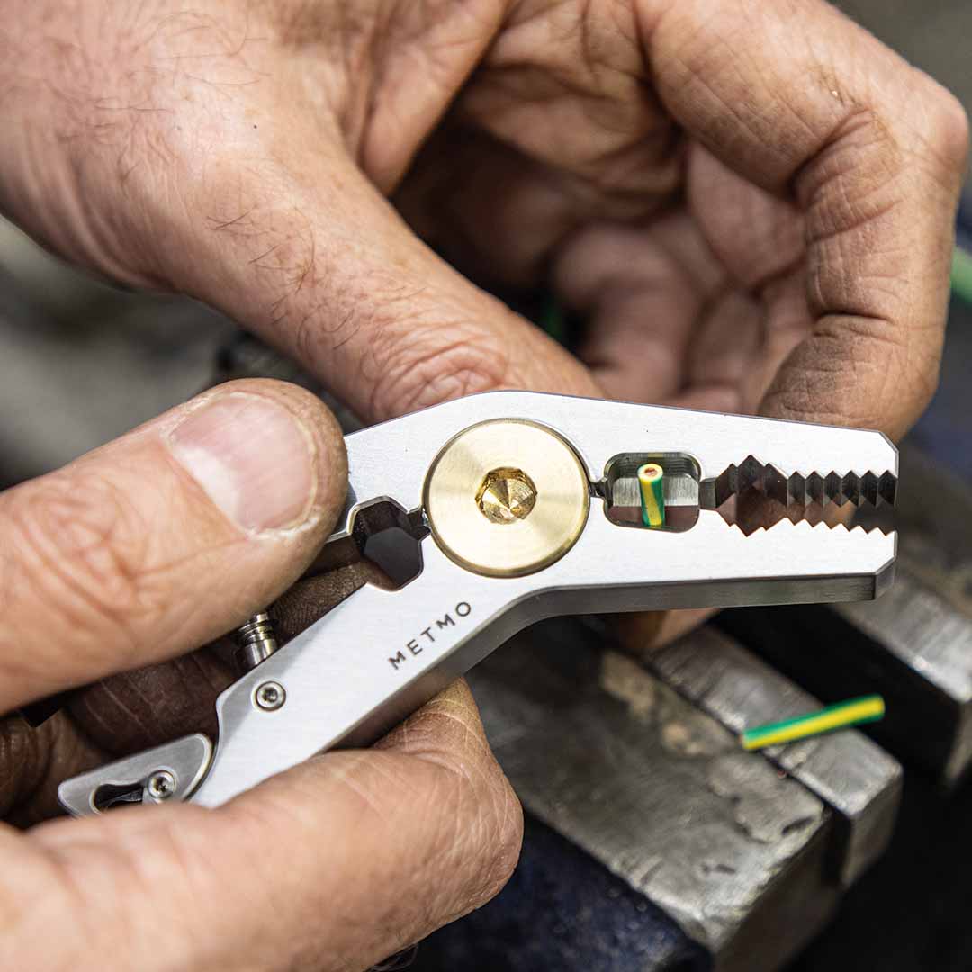Hand holding a multi-tool being used to snip a wire, against a blurred background.