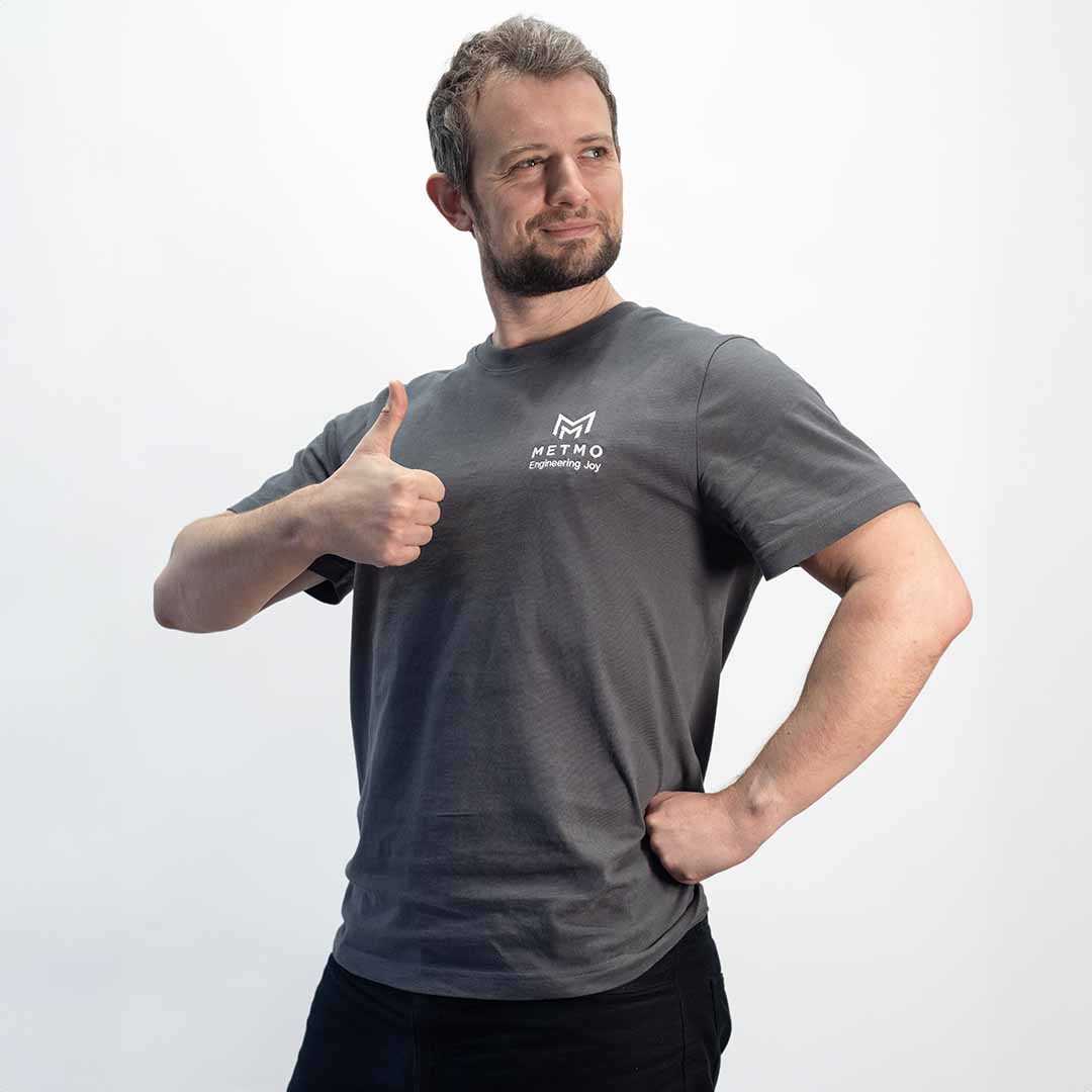 Man wearing a gray MetMo t-shirt, giving a thumbs-up gesture on a white background