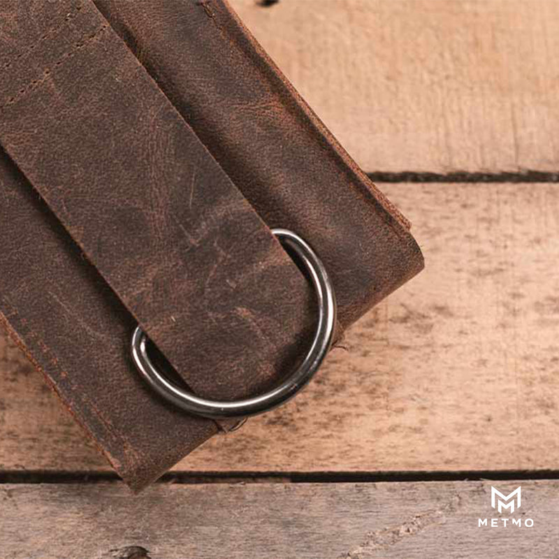 Brown leather pouch with a belt loop and metal D ring on a wooden surface