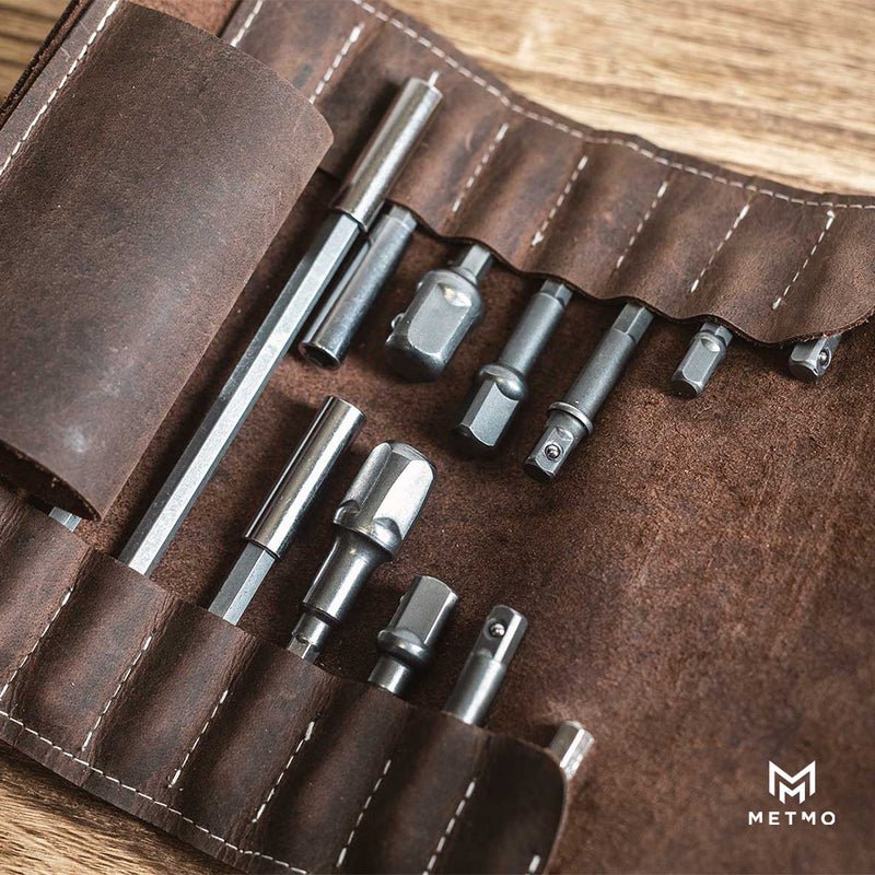 Set of drill bits in a brown leather tool roll on a wooden surface