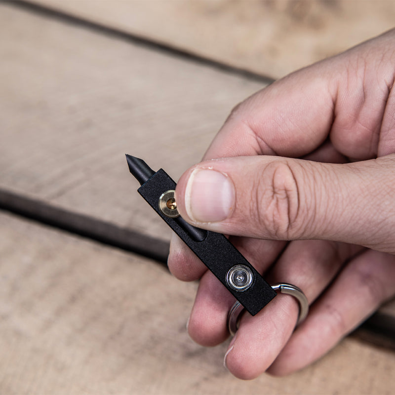 Hand holding a black MetMo Edge multi-tool with a wooden surface background