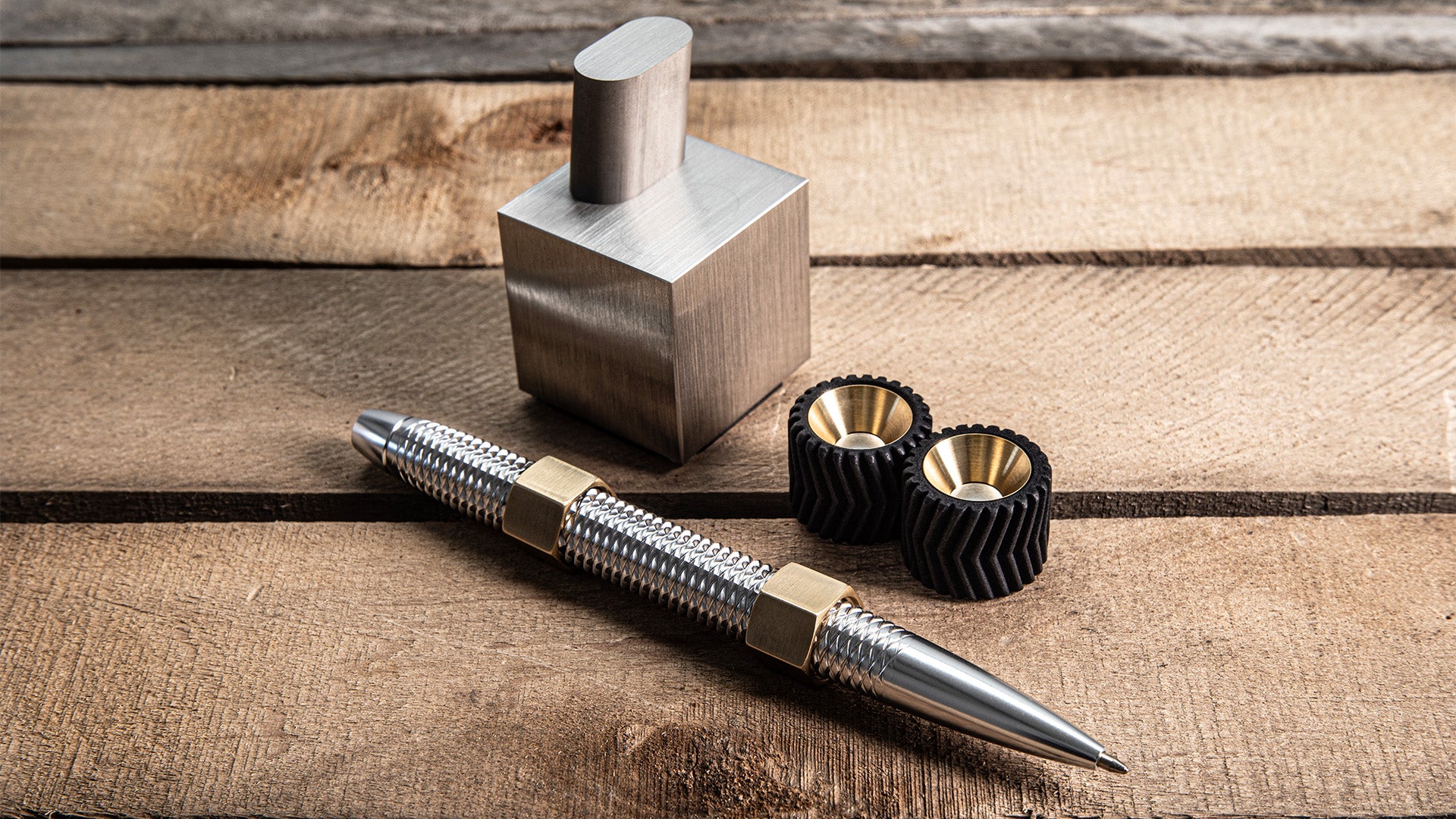 a small collection of highly engineered fidget toys including a pen, gears, and a wire edm cube