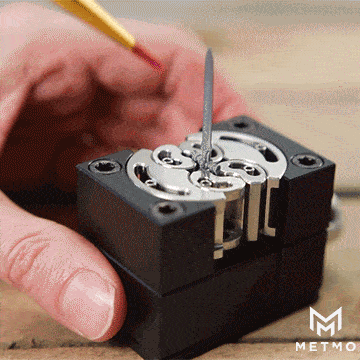 MetMo Fractal Vise in black holding small plastic sword at various angles while painting with red paint fine paintbrush