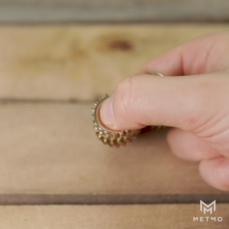 Brass Helico fidget held between thumb and finger being spun in slo-mo